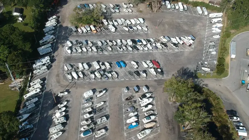 A parking lot filled with various boats, showcasing different sizes and colors, under bright sunlight.